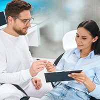 Woman in dental chair signing forms for dentist in white