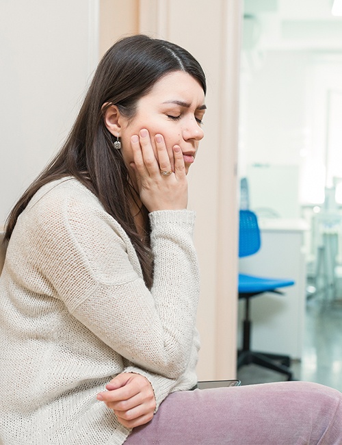 Woman in need of emergency dental care holding cheek in pain