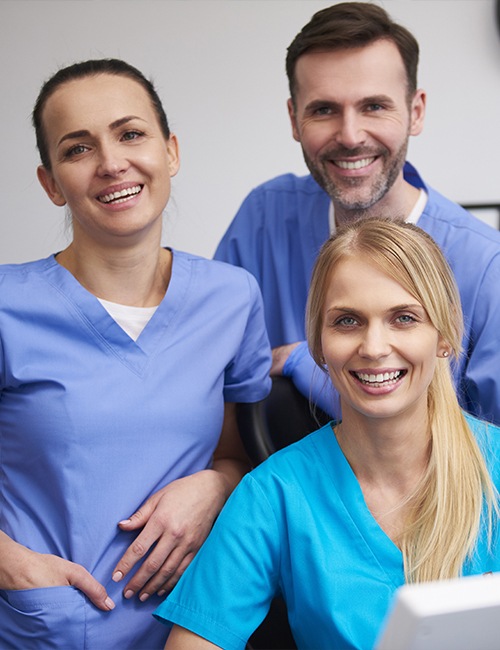 Three smiling dental team members in scrubs