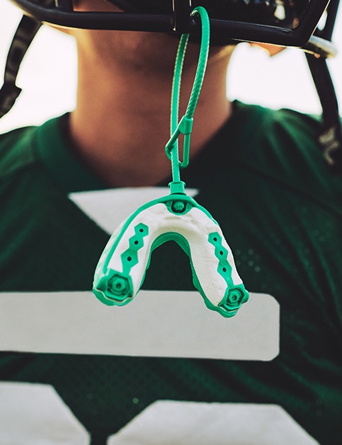 Teen with athletic mouthguard hanging from football helmet