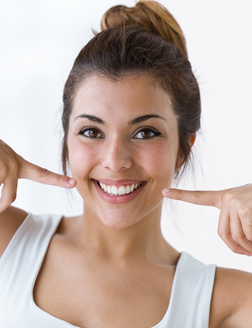 Woman pointing to smile after metal free dental crown treatment