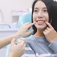 Woman in dentist’s chair pointing to her smile