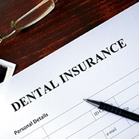 A dental insurance form on a brown desk next to some glasses