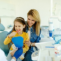 Child sitting on mom's lap while brushing teeth