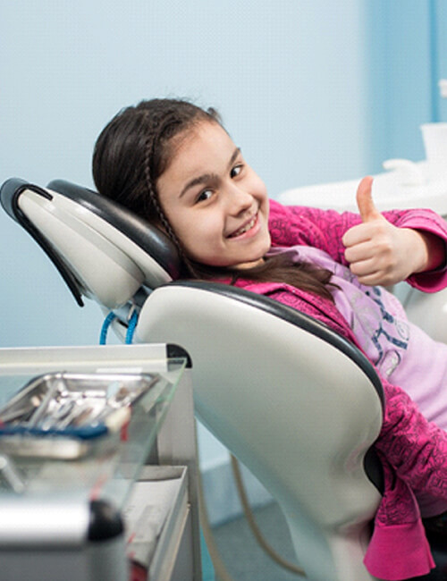 A young girl giving a thumbs-up while seated in the dentist’s chair