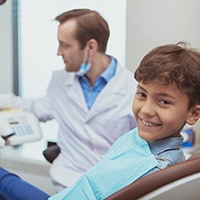 Boy in dental chair smiling with dentist blurry in background