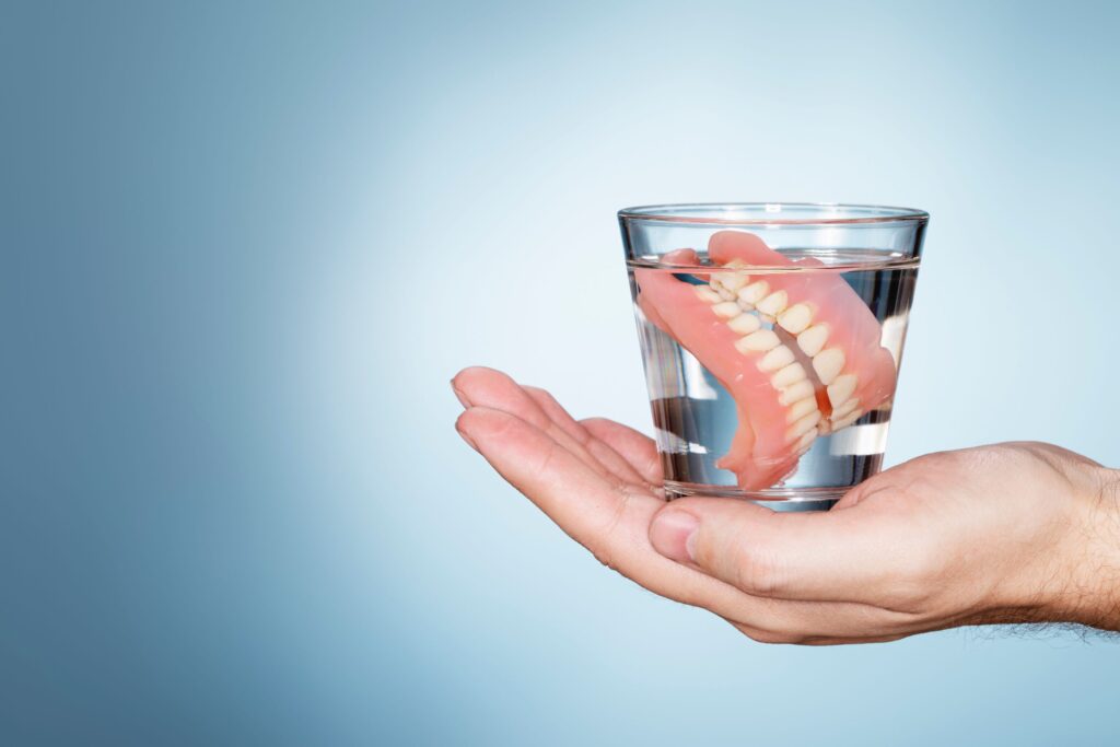 Hand holding glass of clear fluid containing dentures
