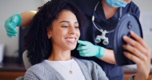 Patient smiling into mirror while sitting in dentist’s chair with dentist nearby.